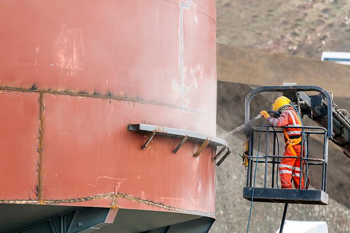 worker sandblasting the exterior of a steel tank