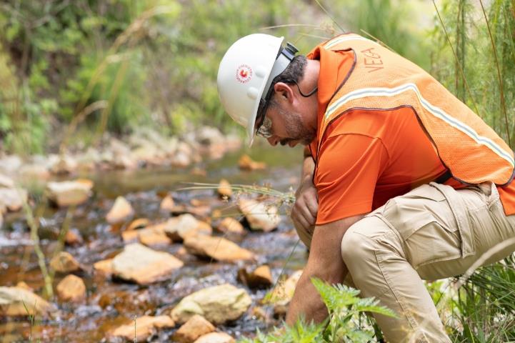 Man in hardhat and safety vest crouching down near a creek