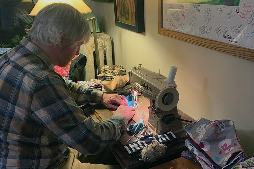 An image of a man creating face masks on a sewing machine.