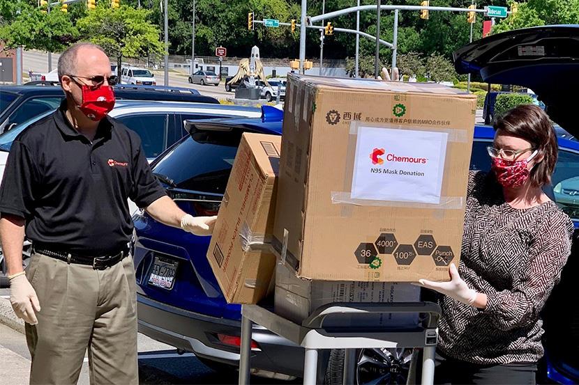 Two people carrying donations boxes in a parking lot.