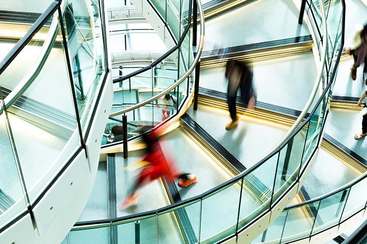 blurred figures walking down a modern steel and glass spiral staircase