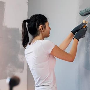 A woman wearing gloves painting wall, at home.