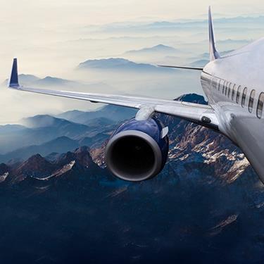 exterior shot of commercial airplane wing and engine flying over mountains