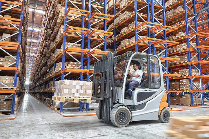 An image of a man operating a forklift in a warehouse moving boxes.
