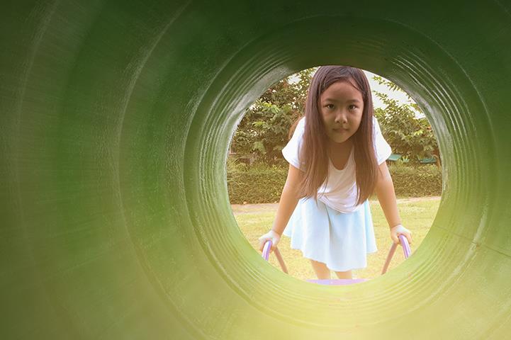 little girl standing in front of and looking into large green play equipment tube