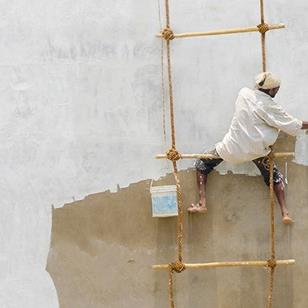 man sitting on rope and bamboo or rattan ladder painting a wall white