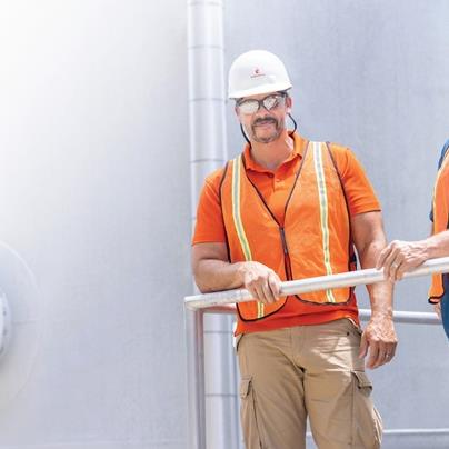 Two employees in hardhats, safety glasses, and high-visibility vests