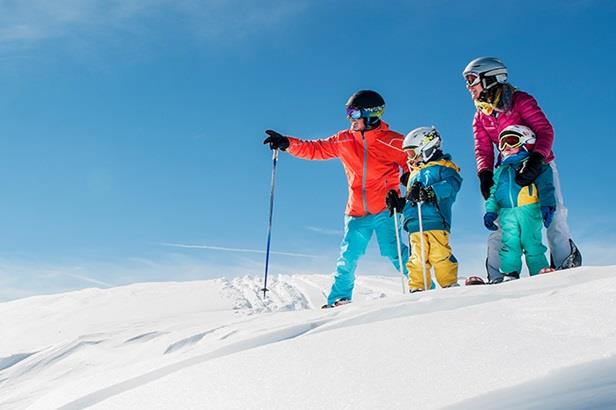 two adults and two children standing at the top of a ski slope