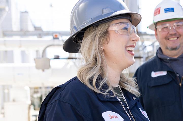 two employees smiling while wearing hardhats