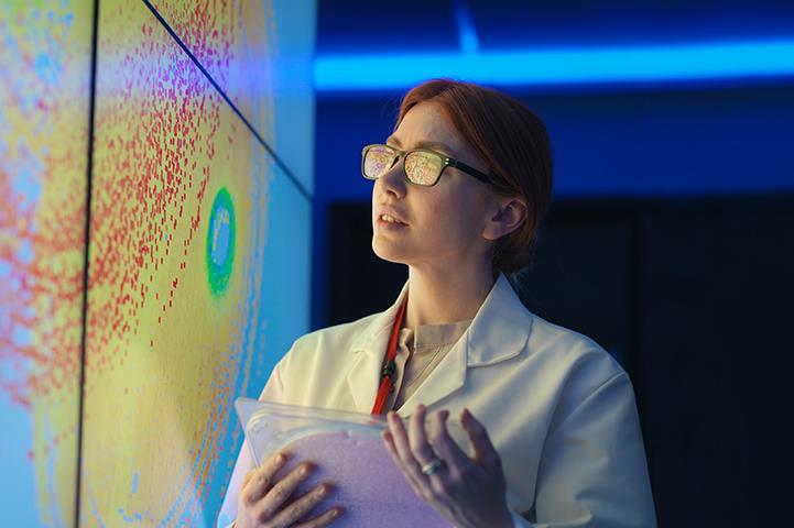 woman in white lab coat holding a silicon wafer in front of a colorful wall