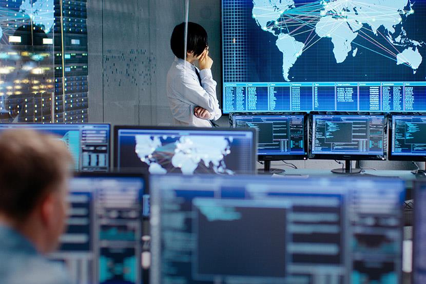person in control room standing in front of large screen that is projecting a world map