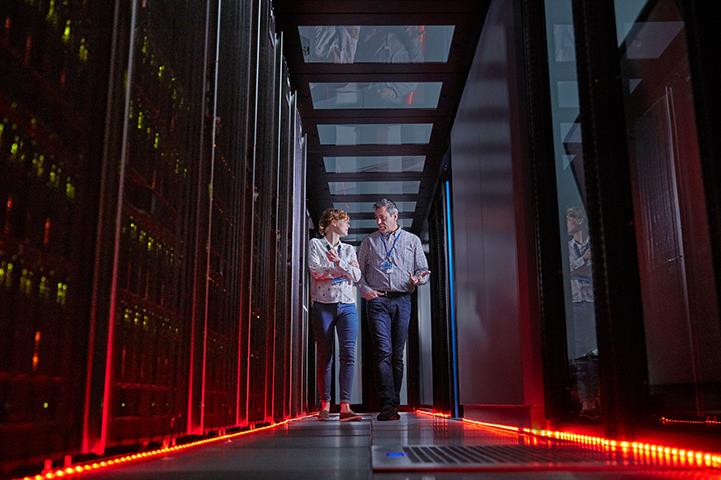 man and woman walking and talking together in a server room that has red floor lights