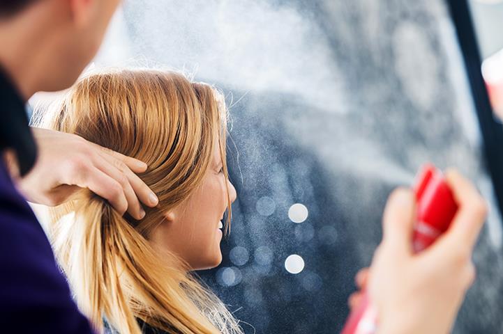 woman in chair at salon person spraying aerosol on hair