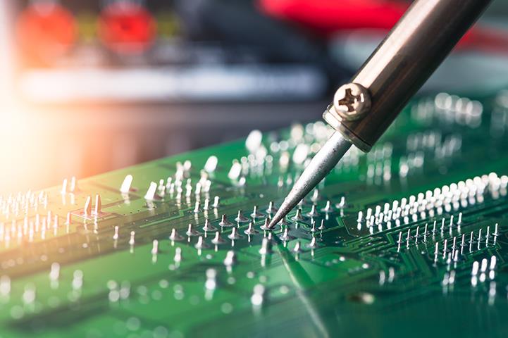 person soldering a green computer circuit board