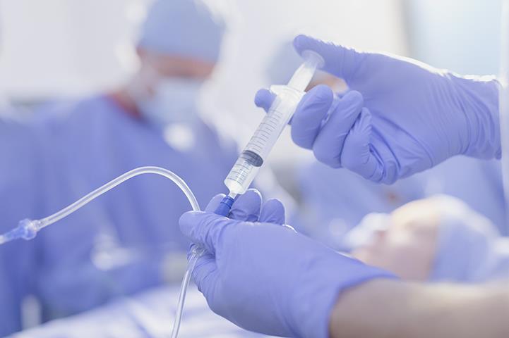 person wearing blue gloves holding syringe and injecting medicine into plastic tubing