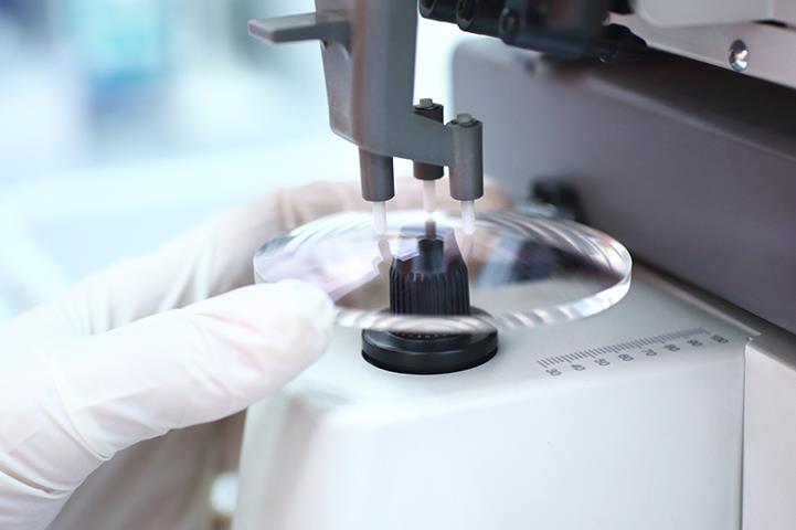 white gloved hand holding eyeglass lens under machine