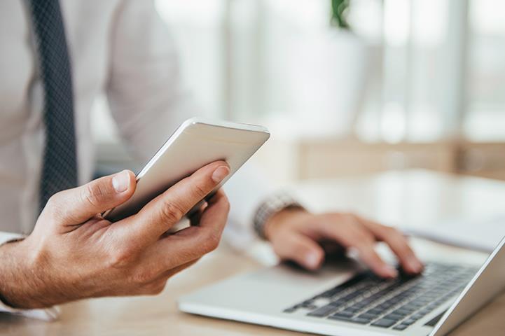 businessman holding phone in right hand left hand resting on a laptop